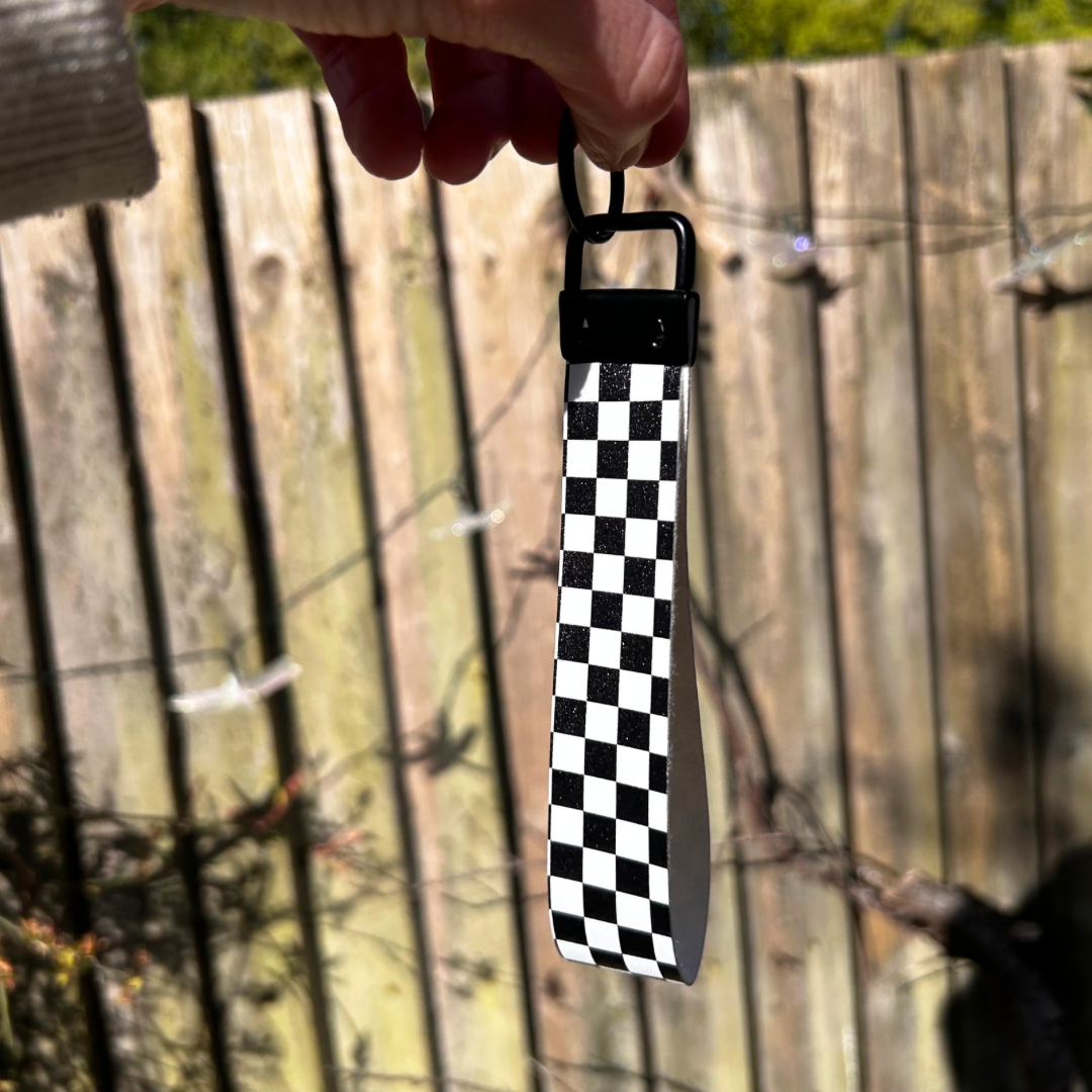 Checkered strap with a black buckle held by a hand against a wooden fence background