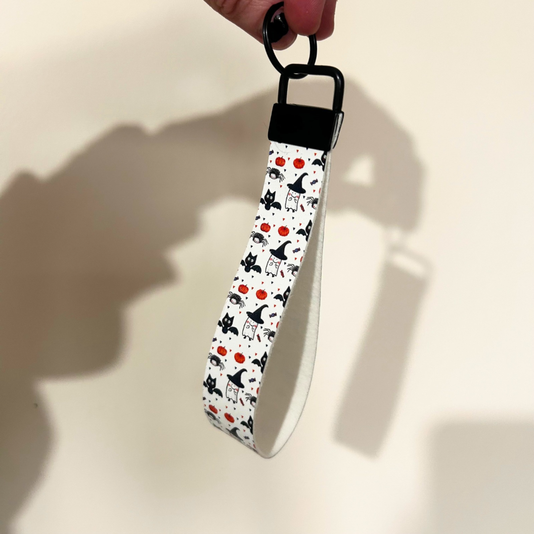 White wristlet with halloween design, cat with bat wings, pumpkin and ghosts, with black hardware 