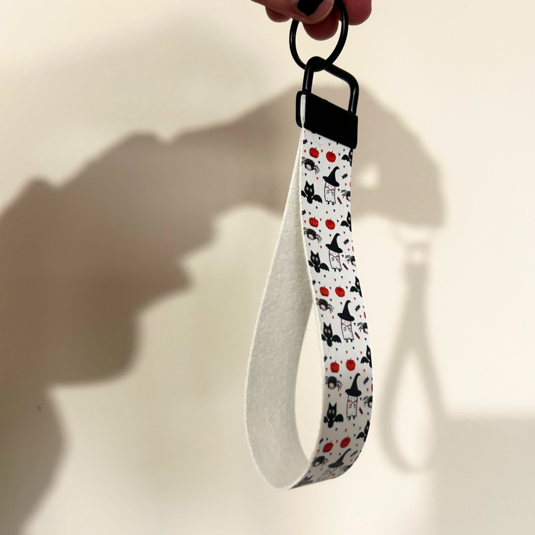 White wristlet with halloween design, cat with bat wings, pumpkin and ghosts, with black hardware 