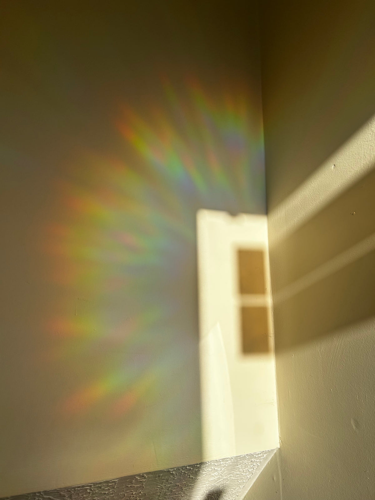 A bright beam of sunlight casting a rainbow spectrum of colors onto a wall in a room corner.