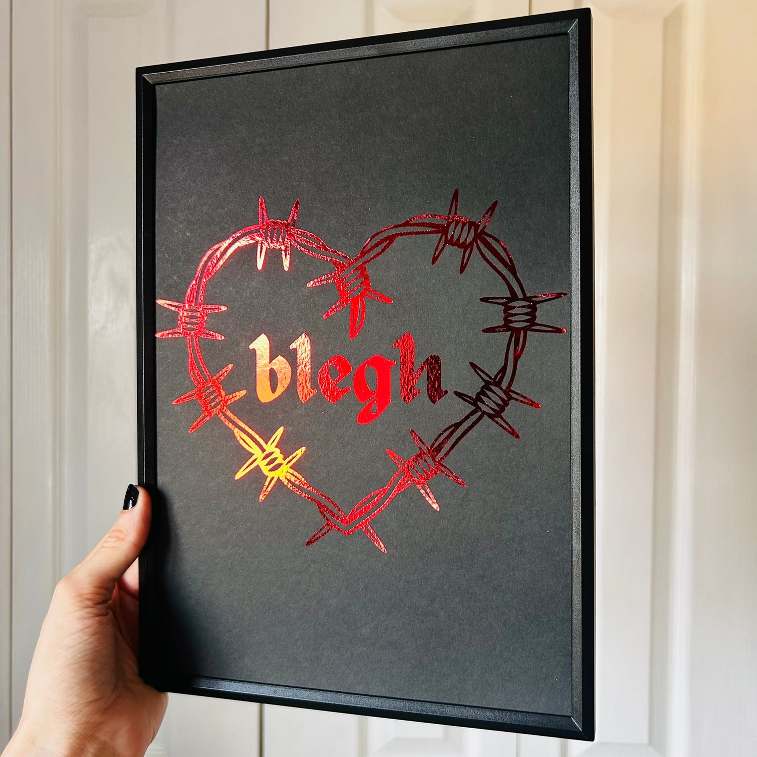 Framed artwork with barbed wire heart design and 'blegh' text on a dark background.