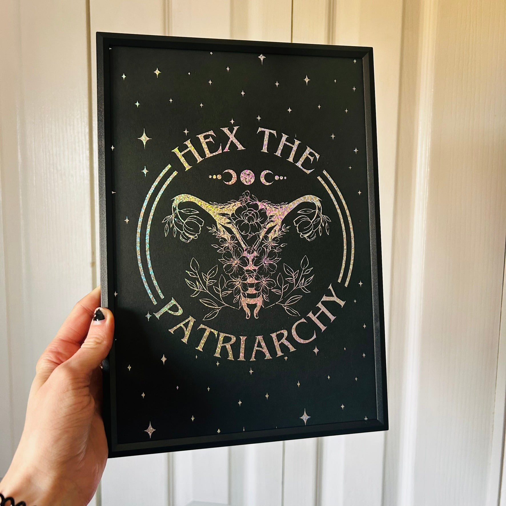 Framed artwork with 'Hex the Patriarchy' text and uterus symbol held by a hand.