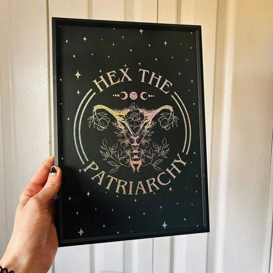 Framed artwork with 'Hex the Patriarchy' text and uterus symbol held by a hand.