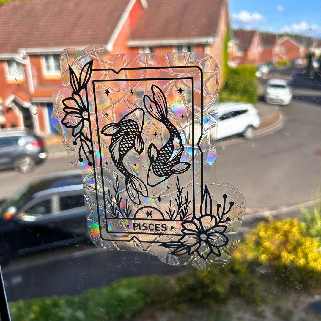 A holographic, crinkle-textured sticker depicting a Pisces tarot card with two fish, applied to a window with a blurred suburban street background.